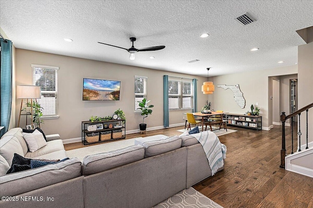 living area with stairway, plenty of natural light, visible vents, and dark wood-style flooring