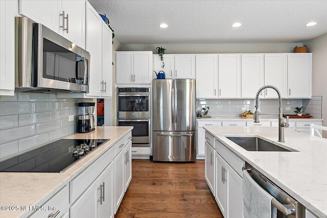 kitchen with light stone countertops, dark wood finished floors, appliances with stainless steel finishes, white cabinets, and a sink