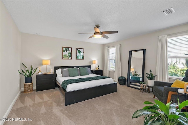 bedroom featuring visible vents, a textured ceiling, baseboards, light colored carpet, and ceiling fan