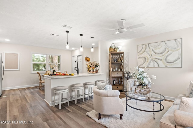 living area with ceiling fan, wood finished floors, visible vents, and baseboards