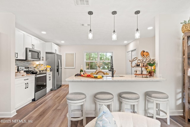 kitchen with visible vents, stainless steel appliances, white cabinets, a kitchen bar, and tasteful backsplash