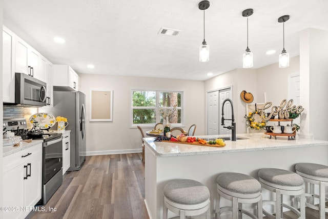 kitchen with visible vents, a breakfast bar, decorative backsplash, wood finished floors, and stainless steel appliances