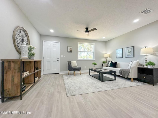 interior space featuring a ceiling fan, light wood-type flooring, visible vents, and a textured ceiling