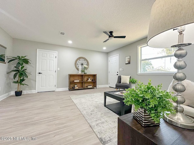 living area featuring visible vents, baseboards, ceiling fan, a textured ceiling, and light wood-style floors