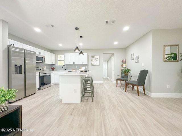 kitchen with a breakfast bar, visible vents, appliances with stainless steel finishes, light wood-type flooring, and decorative backsplash