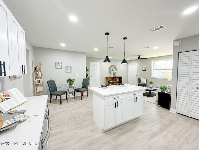 kitchen featuring hanging light fixtures, light wood-style floors, visible vents, and white cabinets