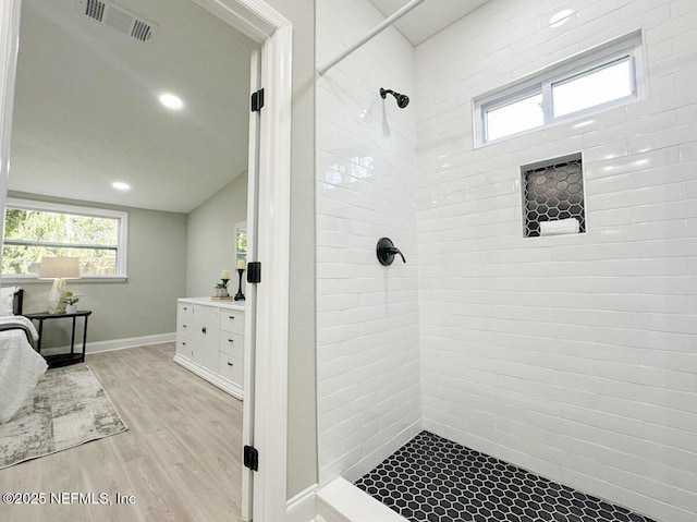 bathroom with visible vents, vaulted ceiling, vanity, wood finished floors, and tiled shower