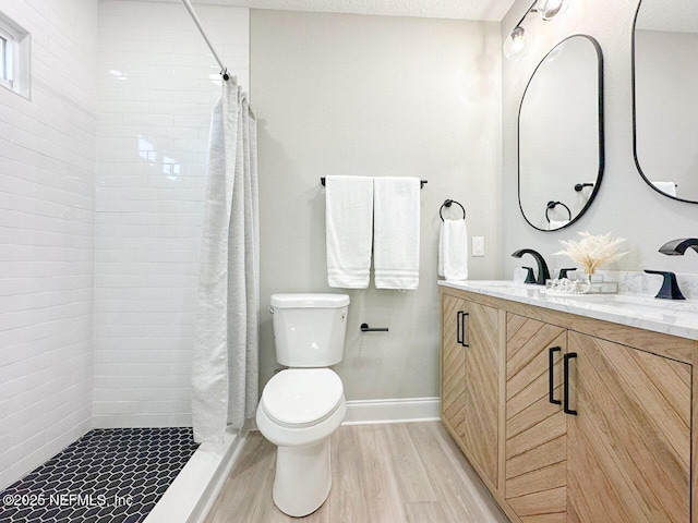 bathroom featuring toilet, a textured ceiling, vanity, wood finished floors, and tiled shower