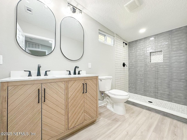 full bathroom featuring visible vents, toilet, a sink, wood finished floors, and tiled shower