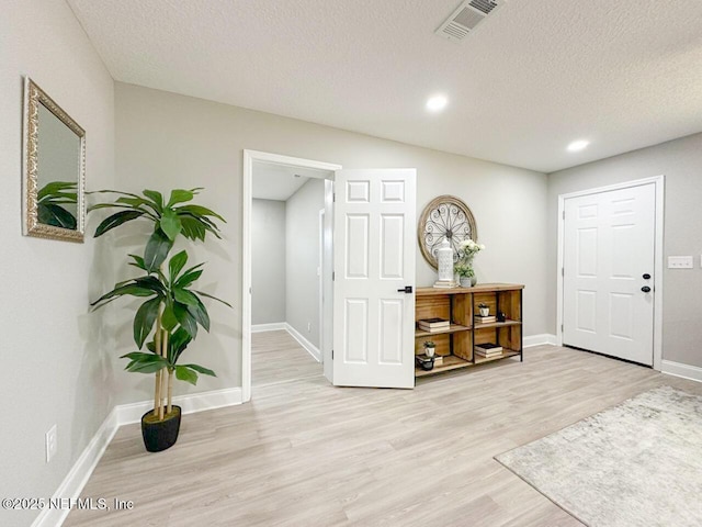 foyer entrance with a textured ceiling, light wood-type flooring, visible vents, and baseboards