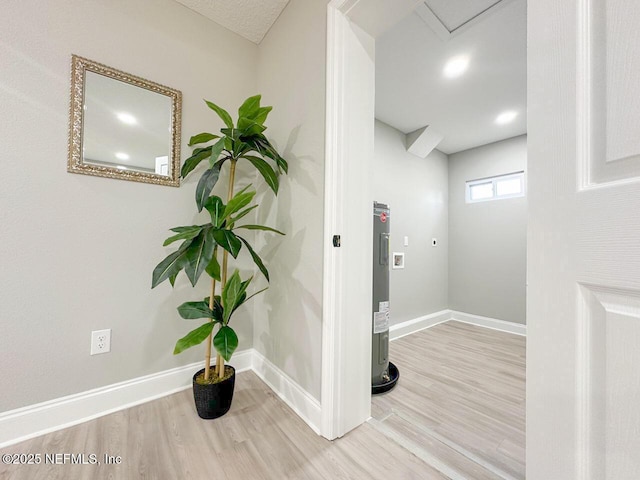 corridor featuring water heater, wood finished floors, and baseboards