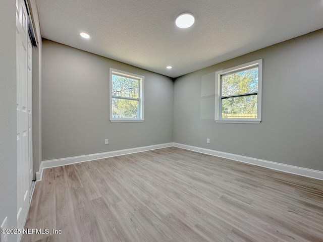 spare room featuring recessed lighting, light wood-style flooring, baseboards, and a textured ceiling