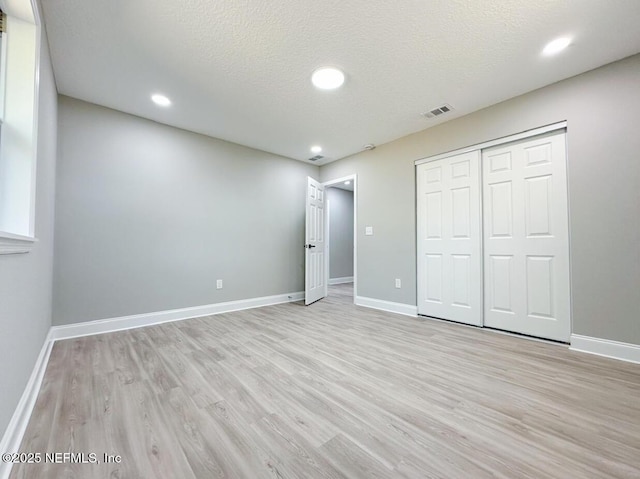 unfurnished bedroom featuring a textured ceiling, light wood-type flooring, visible vents, and baseboards