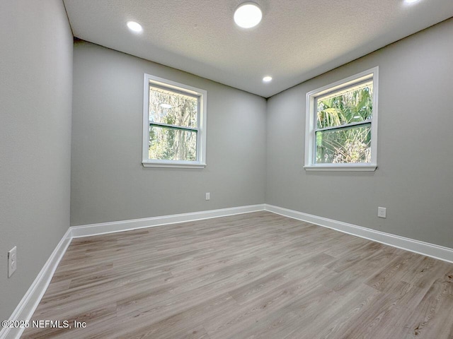 unfurnished room featuring baseboards, plenty of natural light, light wood-style flooring, and a textured ceiling