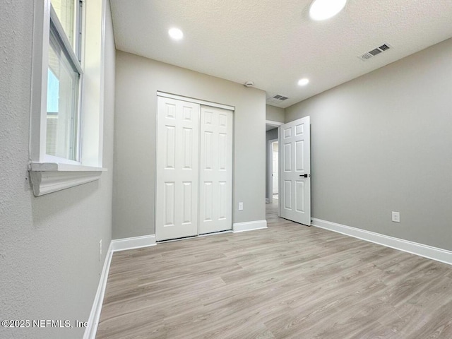 unfurnished bedroom featuring light wood finished floors, baseboards, visible vents, and a closet