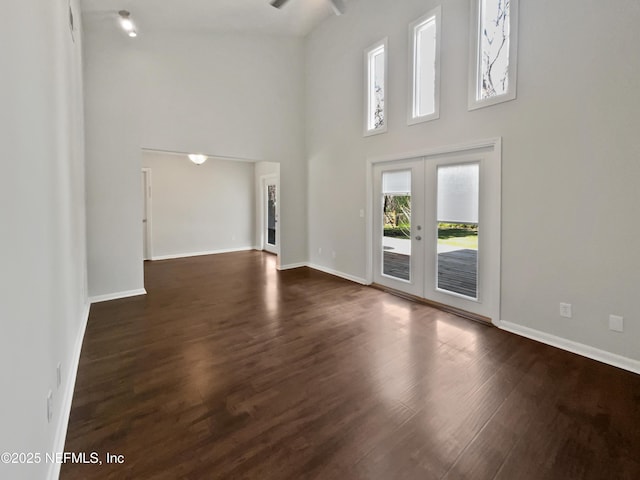 unfurnished living room featuring french doors, baseboards, dark wood-type flooring, and a high ceiling