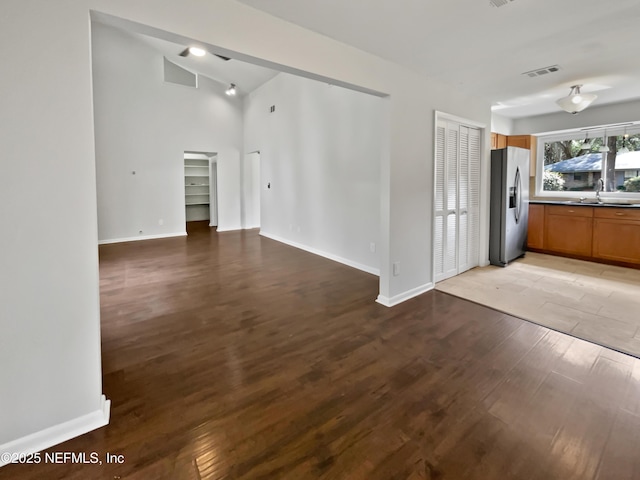 interior space featuring wood finished floors, baseboards, visible vents, a sink, and vaulted ceiling