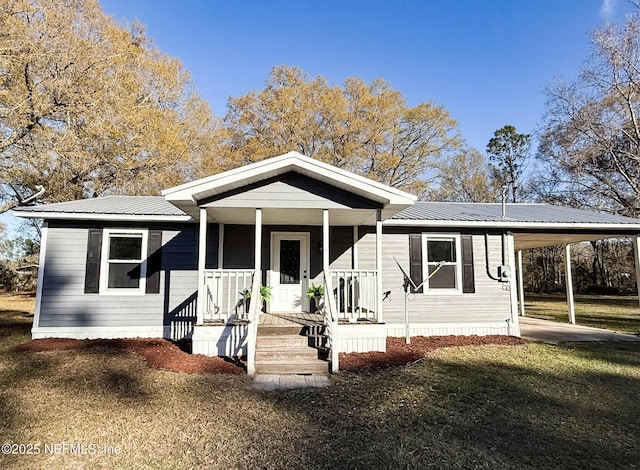 view of front facade with a porch, a front yard, metal roof, and a carport