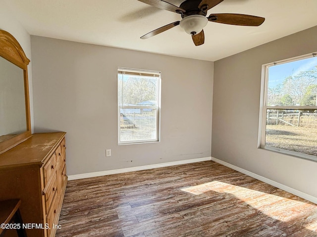 unfurnished bedroom featuring multiple windows, ceiling fan, baseboards, and wood finished floors