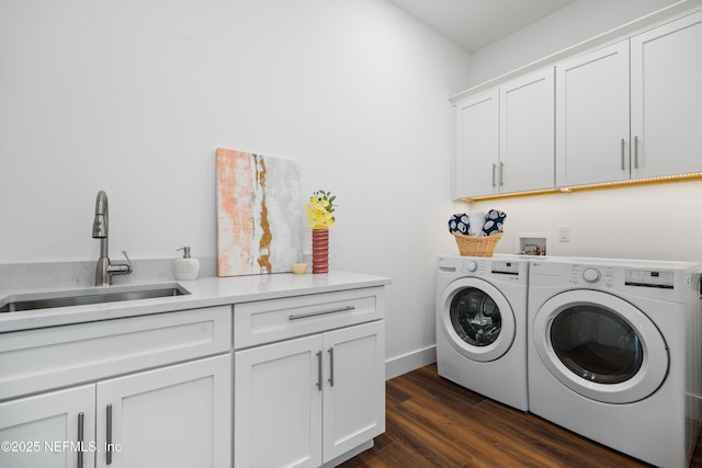 clothes washing area with baseboards, washing machine and clothes dryer, cabinet space, a sink, and dark wood-type flooring