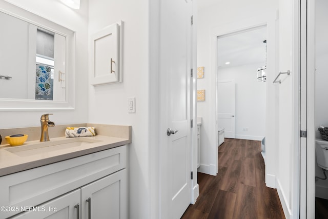 bathroom with toilet, vanity, baseboards, and wood finished floors