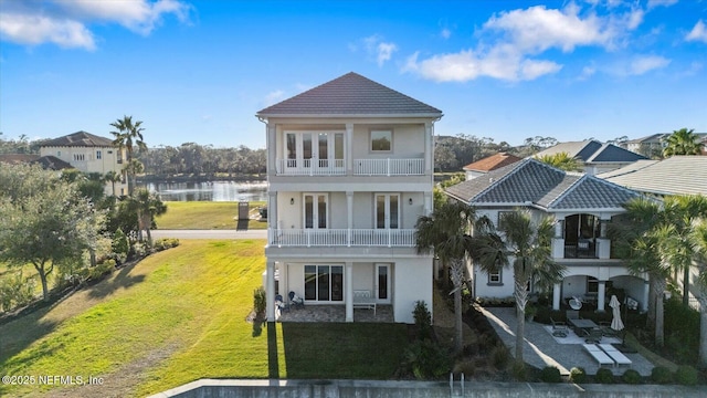 view of front facade with a balcony, a front lawn, french doors, a water view, and a patio area