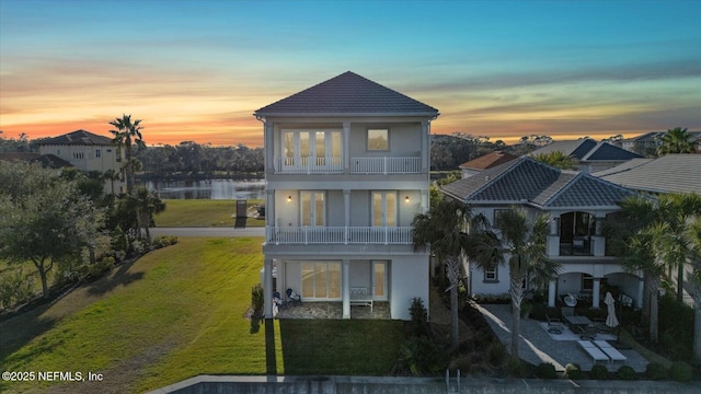 rear view of house featuring a patio, a balcony, a yard, stucco siding, and french doors