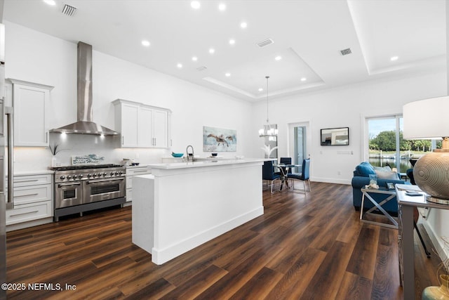 kitchen featuring visible vents, wall chimney exhaust hood, a tray ceiling, and range with two ovens