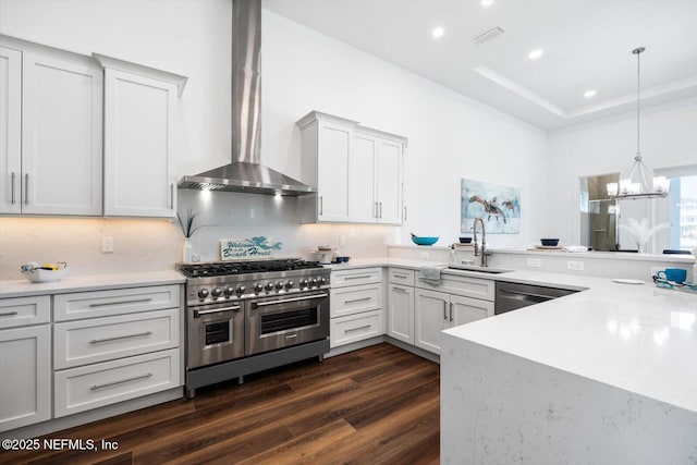 kitchen featuring dark wood finished floors, appliances with stainless steel finishes, a notable chandelier, wall chimney exhaust hood, and a sink