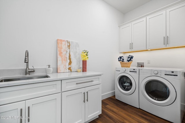 laundry room featuring baseboards, washing machine and clothes dryer, cabinet space, dark wood-style flooring, and a sink