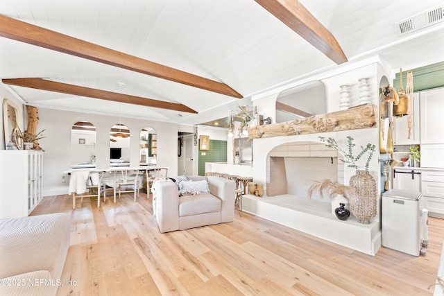 living area featuring lofted ceiling with beams, light wood-style floors, visible vents, and a tile fireplace