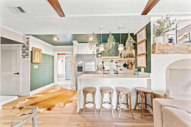 kitchen with light wood finished floors, visible vents, stainless steel refrigerator with ice dispenser, and beamed ceiling