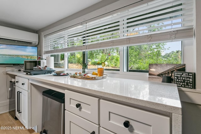 kitchen featuring light stone counters, white cabinets, a wall mounted air conditioner, and light wood-style flooring