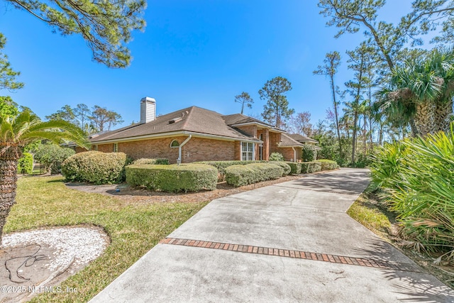 view of side of home with a yard, brick siding, concrete driveway, and a chimney