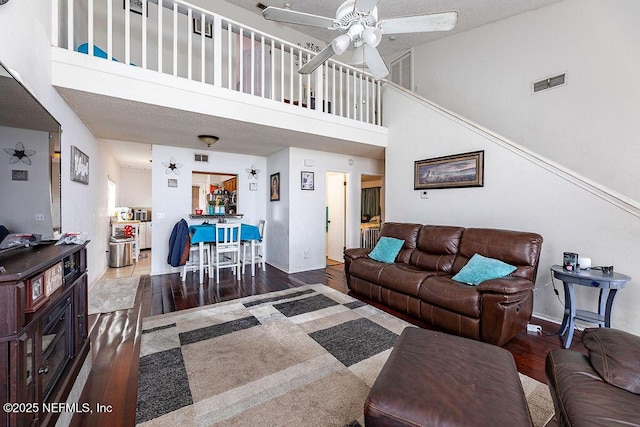 living area featuring a ceiling fan, wood finished floors, visible vents, baseboards, and a towering ceiling