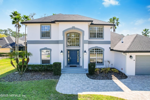 view of front of house featuring roof with shingles, stucco siding, a front lawn, a garage, and decorative driveway