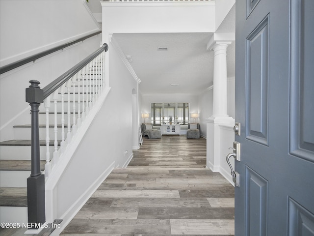 foyer entrance with stairway, wood finished floors, baseboards, ornate columns, and ornamental molding