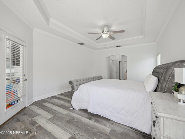 bedroom with visible vents, ornamental molding, wood finished floors, arched walkways, and a raised ceiling