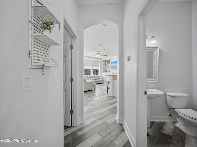 hallway featuring baseboards, arched walkways, and wood finished floors