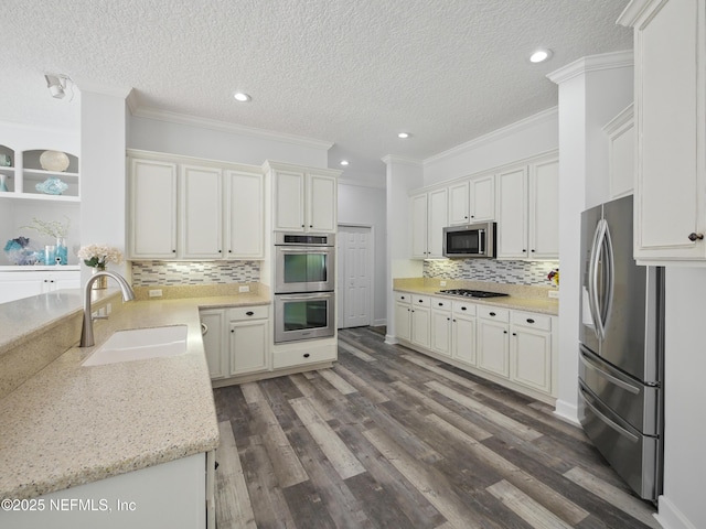 kitchen with dark wood-type flooring, ornamental molding, appliances with stainless steel finishes, and a sink