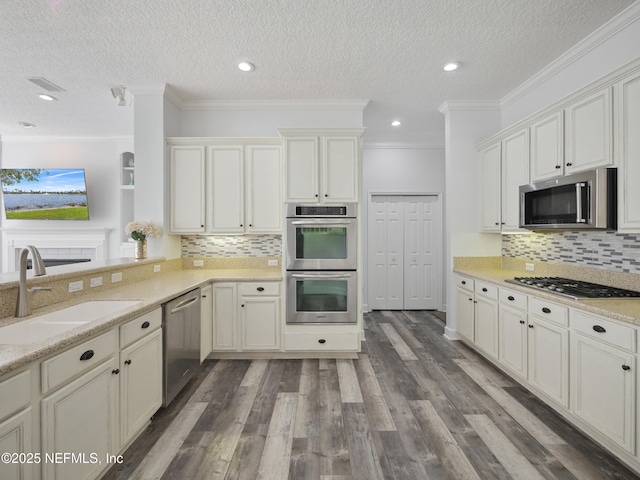 kitchen featuring light stone counters, dark wood finished floors, a sink, appliances with stainless steel finishes, and crown molding