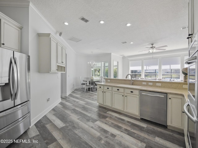 kitchen with a sink, ornamental molding, dark wood-type flooring, stainless steel appliances, and ceiling fan with notable chandelier