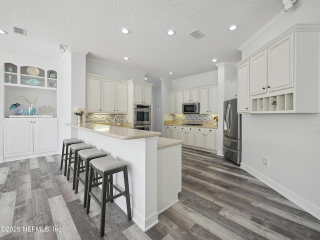 kitchen featuring visible vents, a breakfast bar area, a peninsula, and stainless steel appliances