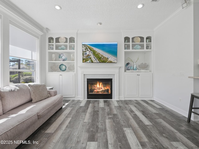 living room with a tiled fireplace, built in features, ornamental molding, wood finished floors, and a textured ceiling