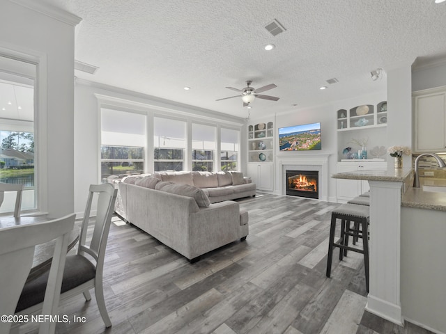 living room featuring visible vents, wood finished floors, a ceiling fan, and a glass covered fireplace