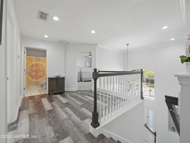 hall with visible vents, an upstairs landing, a textured ceiling, wood finished floors, and recessed lighting