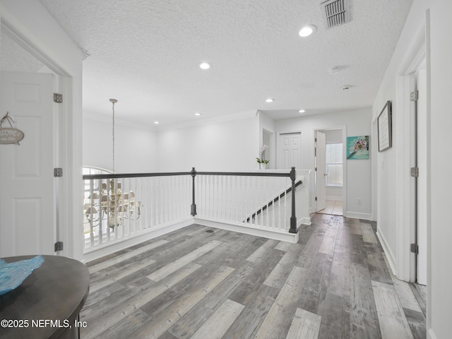 hallway with visible vents, an upstairs landing, a textured ceiling, wood finished floors, and a chandelier