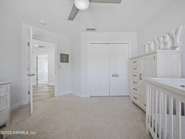 unfurnished bedroom with visible vents, a textured ceiling, a closet, baseboards, and light colored carpet