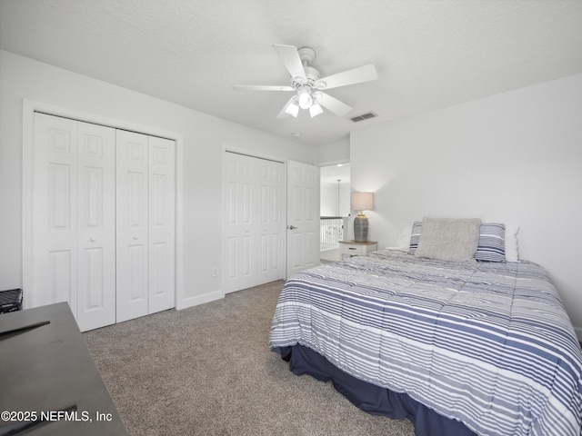 carpeted bedroom with a ceiling fan, visible vents, and two closets