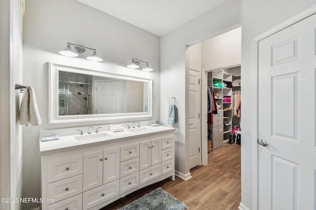 bathroom with wood finished floors, a sink, a shower, double vanity, and a walk in closet